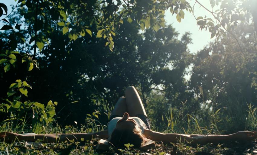 Nő hason fekszik a park fűjén, nyitott könyvvel olvas, relaxál a természetben